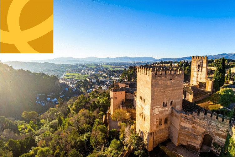 A wide view of the Alhambra fortress in Granada, Spain, with surrounding greenery and hills under a clear blue sky; a yellow abstract logo overlays the top left corner.