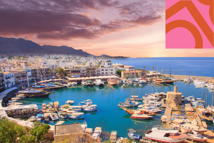 Scenic harbour filled with boats and surrounded by buildings at sunset, with mountains in the background and a pink-red abstract design overlay in the top right corner.