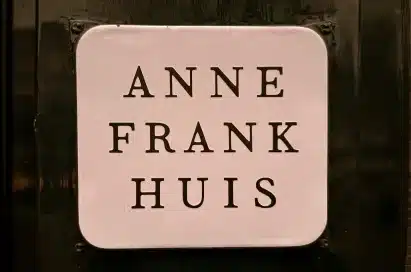 White sign with black text reading "ANNE FRANK HUIS" mounted on a dark background.