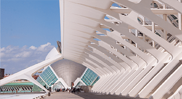 Wide-angle view of a modern white architectural structure with geometric patterns and people walking underneath, likely part of an urban complex.