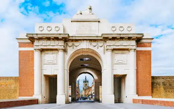 A large stone memorial archway with intricate carvings, red brick sides, and a central passage leading to a street with buildings visible in the background.