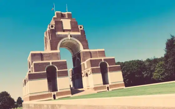 Large brick and stone memorial arch with lawns and trees, under a clear blue sky.