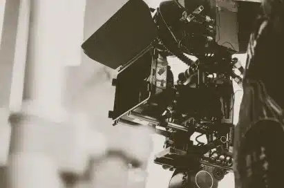A close-up of a professional film camera set-up on set, featuring various attachments and equipment in a monochrome tone.