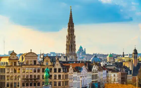 Cityscape of Brussels featuring historic buildings, a statue in the foreground, and the tall spire of the Town Hall rising above the skyline—a striking scene for those inspired by science trips to Iceland and beyond.