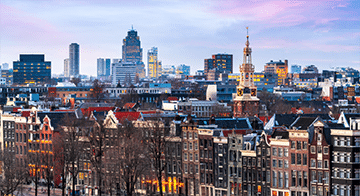 Skyline view of Amsterdam featuring historic buildings in the foreground and modern high-rise structures in the background under a partly cloudy sky.