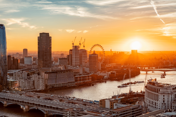 A cityscape of London at sunset, featuring the River Thames, bridges, high-rise buildings, and the London Eye in the background.