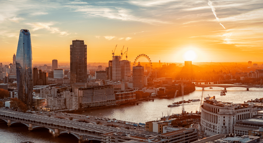 A cityscape of London at sunset, featuring the River Thames, bridges, high-rise buildings, and the London Eye in the background.