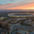 Aerial view of a large, circular office building surrounded by trees and smaller buildings at sundown.