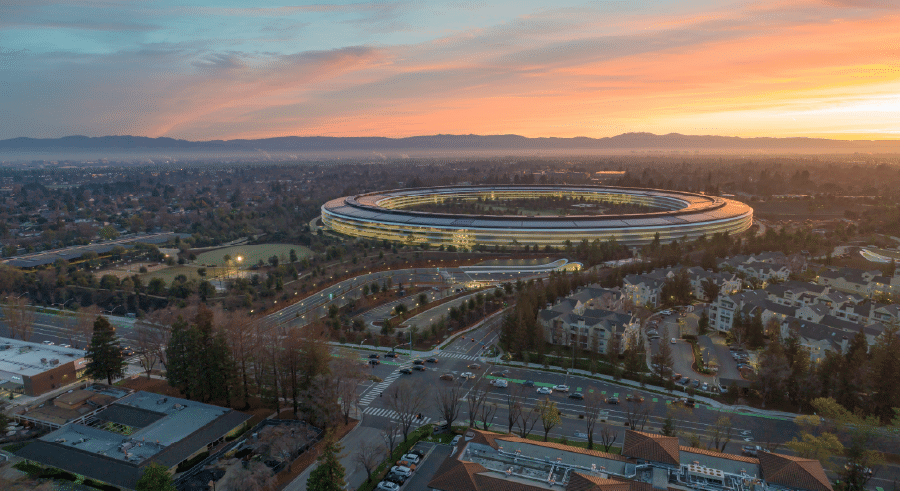 Aerial view of Apple's circular headquarters, Apple Park, in Cupertino, California, surrounded by trees and buildings at sundown.