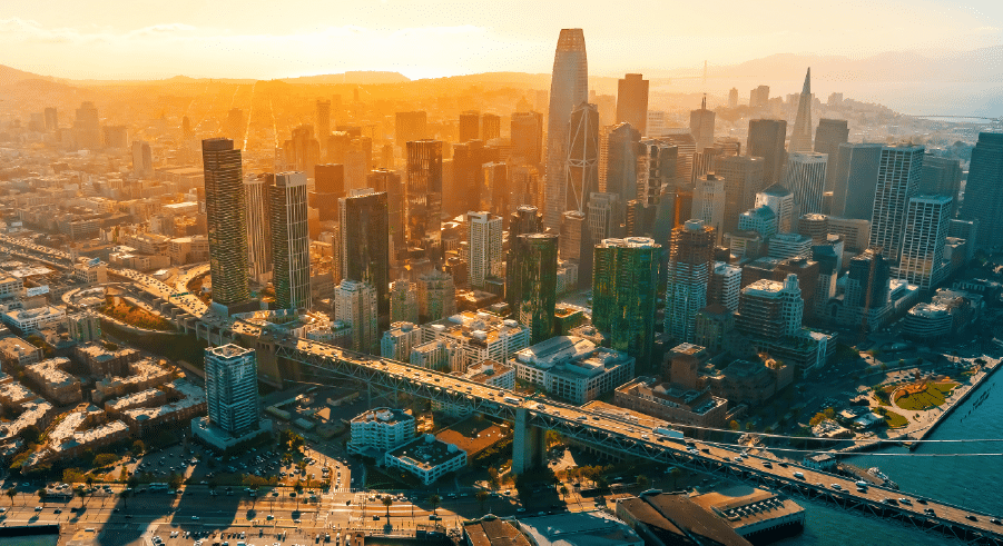 Aerial view of city centre San Francisco with skyscrapers, motorways, and the waterfront at sunset.