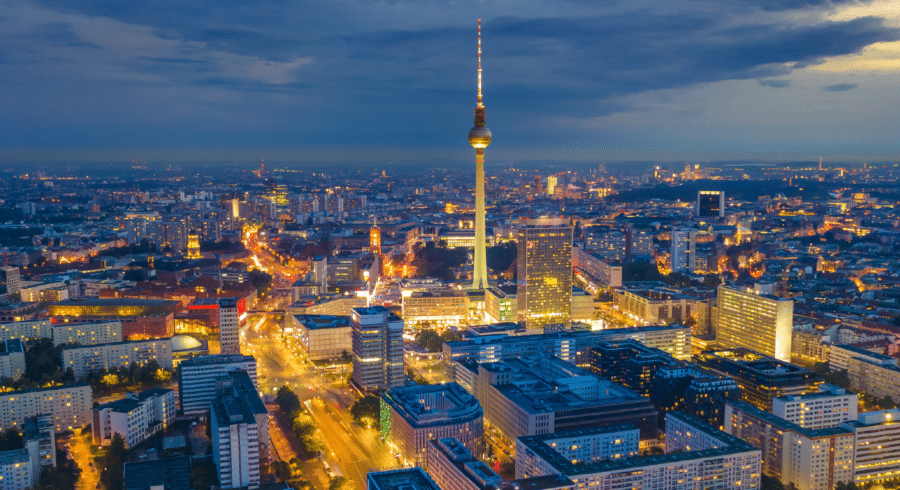 Aerial view of Berlin cityscape at dusk with illuminated buildings and the Fernsehturm TV tower prominent in the centre.