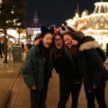 Three people stand close together and smile on a well-lit street at night in what appears to be a theme park.