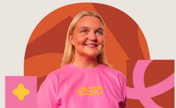 A person with blonde hair wearing a pink shirt with "esto" printed on it stands in front of an abstract orange and pink background.