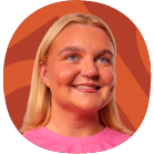 A woman with long blonde hair and a pink shirt smiles in front of an orange patterned background.
