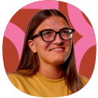 Person with long brown hair and glasses, wearing a yellow shirt, smiling in front of a red and pink abstract background.