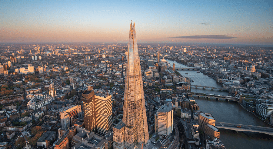 Aerial view of The Shard skyscraper in London, surrounded by city buildings and the River Thames at sunset.