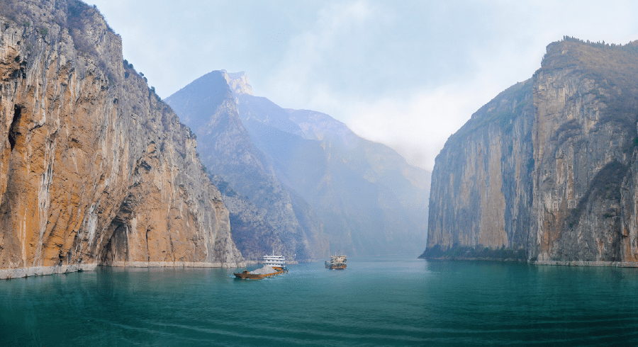 Tour boats travel along a wide river flanked by steep, rocky cliffs and misty mountains in the background—a scene reminiscent of science trips Iceland adventurers dream of.