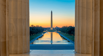 View of the Washington Monument and Reflecting Pool at sunrise, framed by columns of the Lincoln Memorial in Washington, D.C.