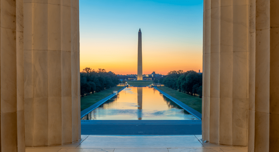 View of the Washington Monument and Reflecting Pool at sunrise, framed by columns of the Lincoln Memorial in Washington, D.C.