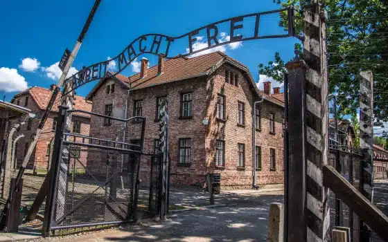 The entrance gate to Auschwitz concentration camp with the "Arbeit Macht Frei" sign above, brick buildings and a clear sky in the background.