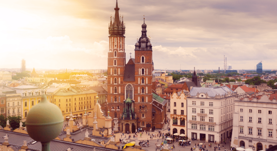 Aerial view of St Mary’s Basilica and surrounding historic buildings in Kraków’s Main Market Square, under a partly cloudy sky with sunlight.