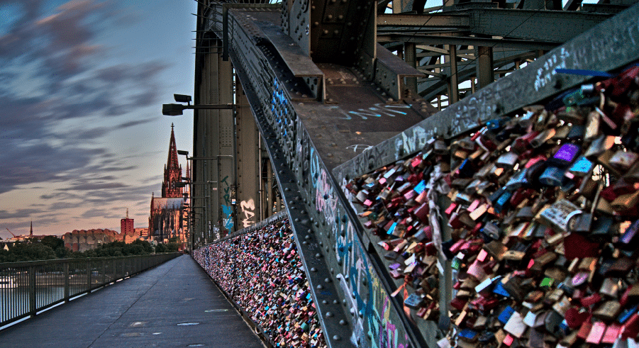 A bridge covered in thousands of colourful padlocks with a view of a large cathedral in the background during sunset.