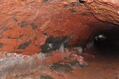 Tunnel with reddish-brown, rocky walls and ceiling, featuring patches of darker rock and a rough, uneven floor—an ideal spot for science trips in Iceland.