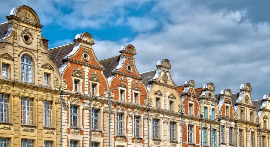 Row of historic European buildings with ornate gabled roofs and decorative façades under a partly cloudy sky.