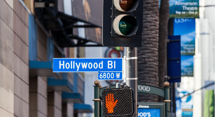 A street sign for Hollywood Blvd and 6800 W, with a pedestrian signal showing a red hand and a traffic light above it.