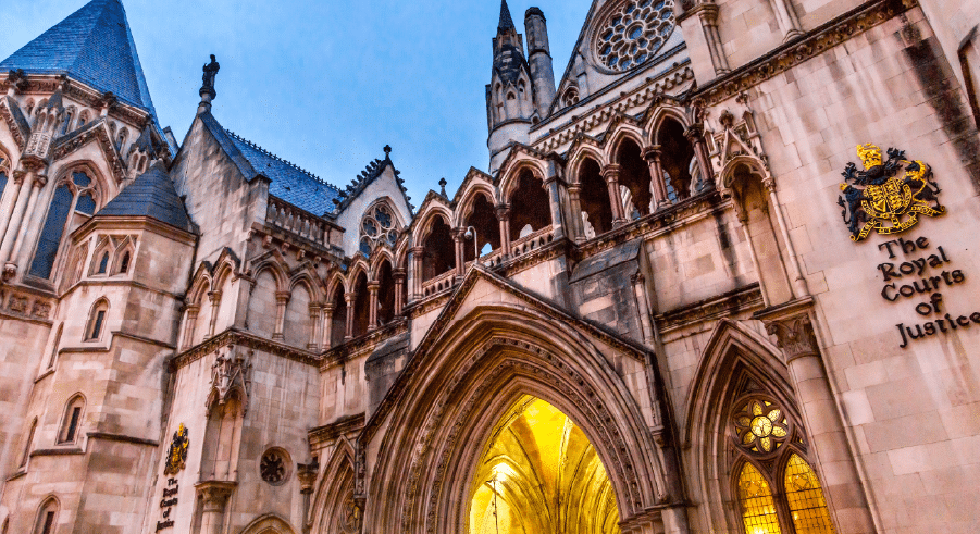 The exterior of the Royal Courts of Justice in London, showing its ornate Gothic-style architecture and illuminated arched entrance.