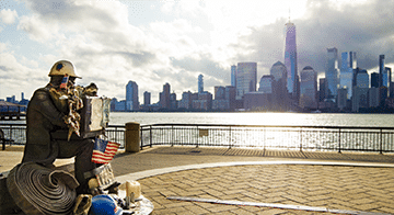 A statue of a construction worker sitting with tools and an American flag, overlooking the Manhattan skyline across the Hudson River.