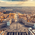 Aerial view of St. Peter's Square in Vatican City, featuring the central obelisk, colonnades, and surrounding cityscape under a partly cloudy sky.