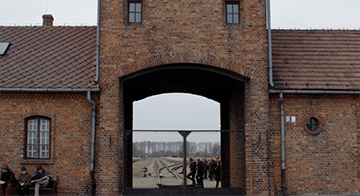The entrance gate and railway tracks leading into Auschwitz concentration camp, with visitors visible in the background.