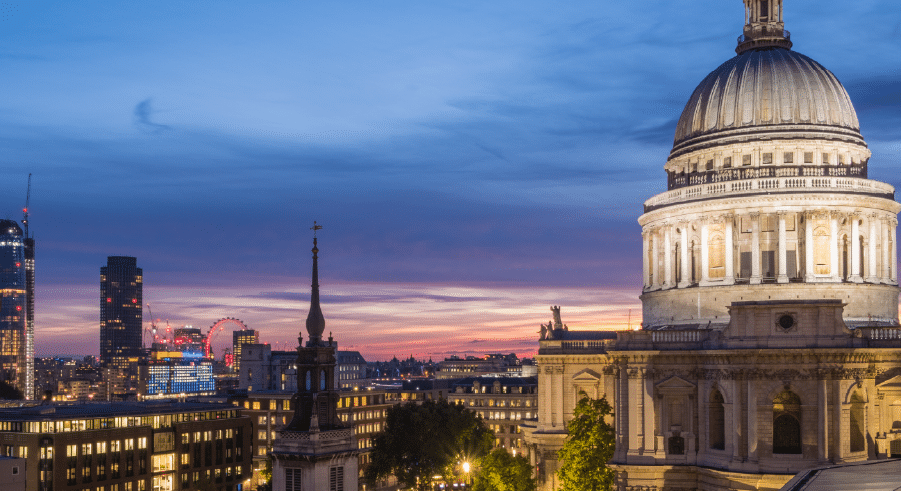View of London skyline at dusk featuring the dome of St Paul’s Cathedral on the right, with city buildings and the London Eye visible in the background.