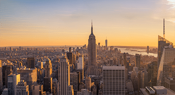 New York City skyline at sunset with the Empire State Building in the centre and other skyscrapers surrounding it.