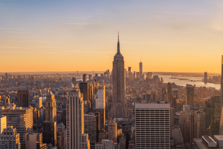 New York City skyline at sunset, featuring the Empire State Building in the centre and various skyscrapers under an orange sky—the perfect view for science trips New York enthusiasts to admire.
