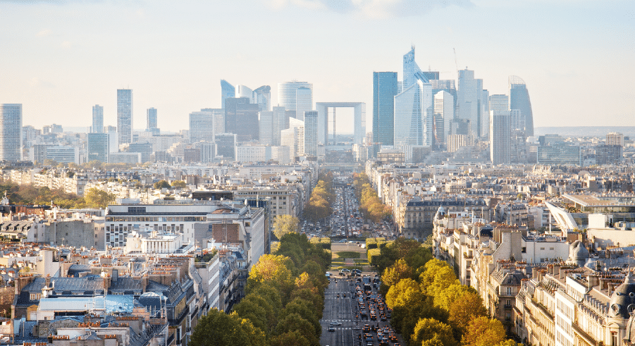 A wide view of Paris with the modern skyscrapers of La Défense in the background and tree-lined streets leading through the city.