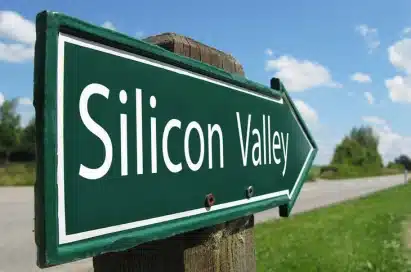 A green directional road sign with the words "Silicon Valley" points to the right, with a road and sky in the background.