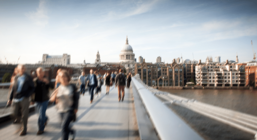 People walking on the Millennium Bridge in London with St. Paul’s Cathedral and city buildings visible in the background.