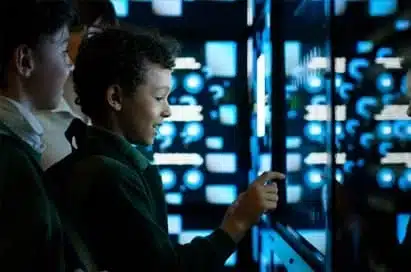 A group of children interact with a touchscreen display showing blue and white digital graphics in a dark room.