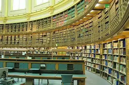 A large, circular library reading room with curved shelves filled with books and rows of desks with computers.