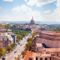 Aerial view of Washington, D.C. featuring the US Capitol building in the background and tree-lined streets in the foreground on a sunny day.
