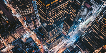 Aerial view of city skyscrapers and illuminated streets at night, showing dense urban development and busy junctions.