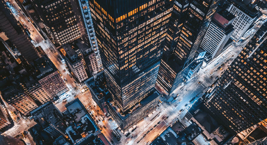 Aerial view of a city at night with illuminated skyscrapers, streets, and junctions forming a grid pattern.