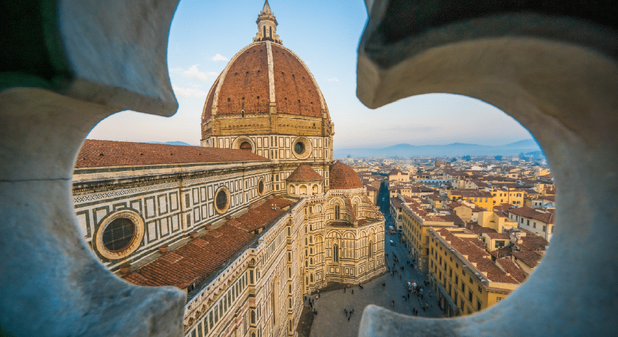 View of Florence Cathedral’s dome and cityscape, framed by architectural stonework, under a clear sky at sundown.