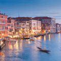 View of the Grand Canal in Venice at dusk, with historic buildings lining the water and boats moving along the canal.