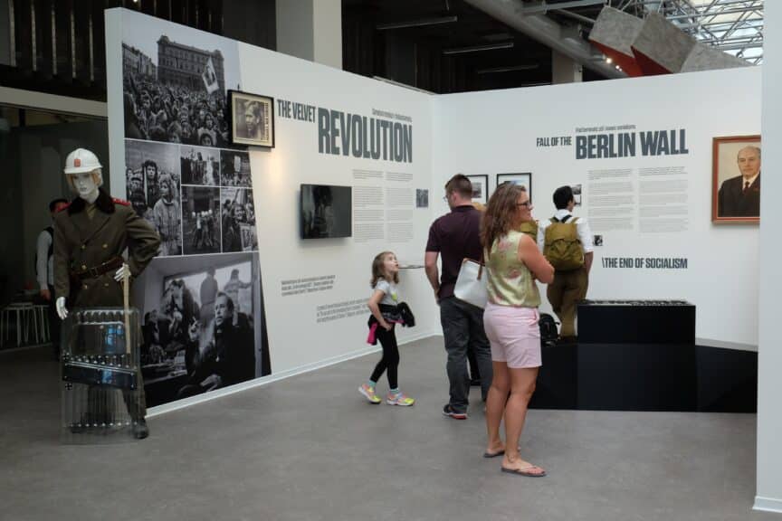 People view photos, text panels, and mannequins in a museum exhibition about the Velvet Revolution and the fall of the Berlin Wall.