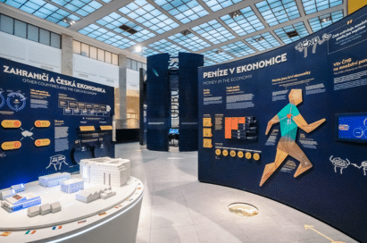 Museum exhibition on economics with information panels, diagrams, and a geometric human figure; texts are in Czech and English.