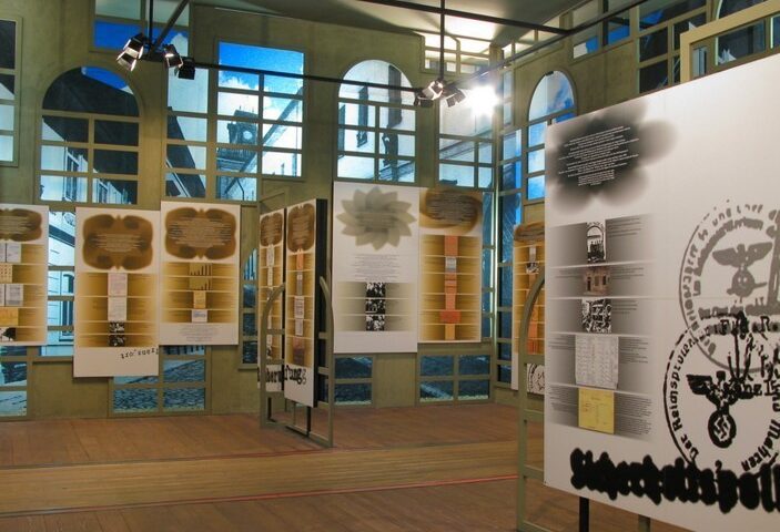 Art exhibition with modern informational panels displayed in a room with wooden floors, large windows, and track lighting.