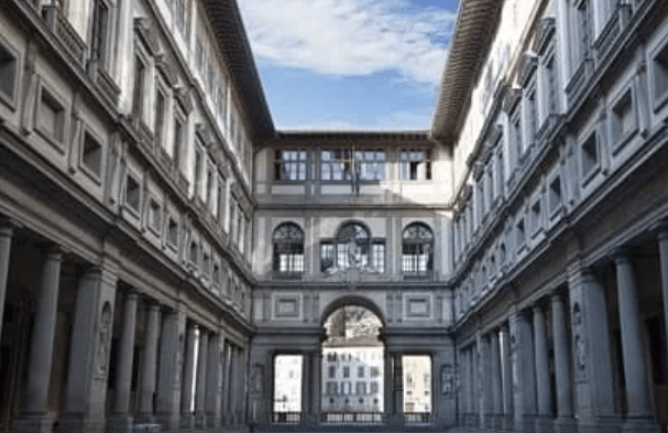 Symmetrical view of the Uffizi Gallery’s exterior corridor in Florence, Italy, with arches, columns, and a blue sky visible above.